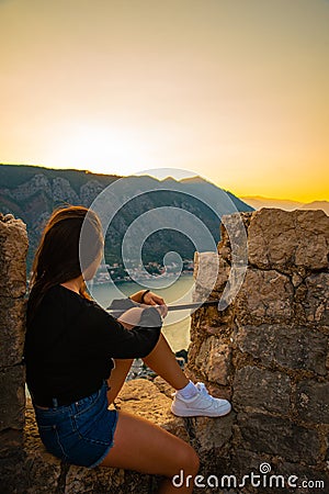 Woman sitting on top of hill on sunset with beautiful view of kotor Stock Photo