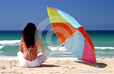 Woman sitting under colorful parasol on white sandy beach Stock Photo