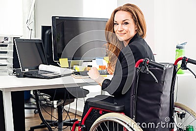 Woman Sitting In Wheelchair Working In Modern Office Stock Photo