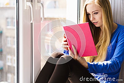 Woman sitting on window sill reading book at home Stock Photo