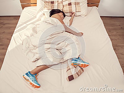 Woman sleeps in bed with her running shoes on Stock Photo