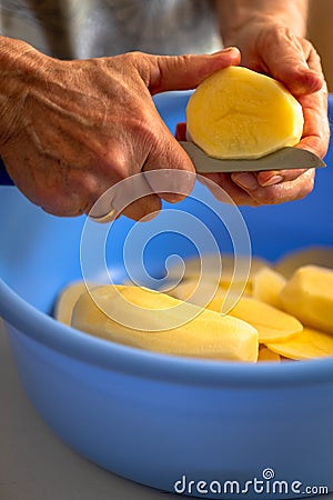 Fresh tasty potatoes cut into perfect round slices. Woman sliced potatoes in round shape with knife in a blue bowl Stock Photo