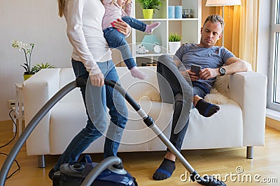 Woman with small child doing housekeeping while man sitting in couch Stock Photo