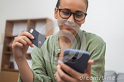 woman smiles while efficiently managing credit card payment near her phone during online shopping. Stock Photo