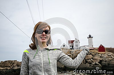 Woman smiles and holds the Nubble Lighthouse in a forced perspective view Stock Photo