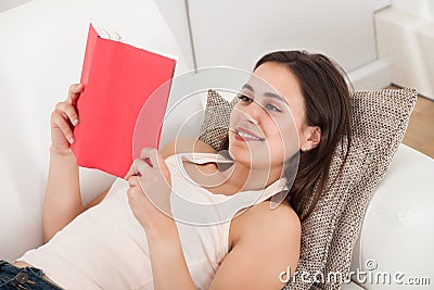 Woman Smiling While Reading Book On Sofa Stock Photo