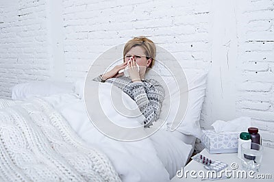 woman with sneezing nose blowing in tissue on bed suffering cold flu virus symptoms having medicines tablets pills Stock Photo