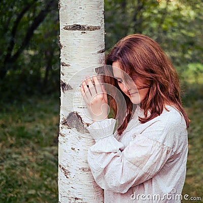 Woman snuggles against birch tree in summer park Stock Photo
