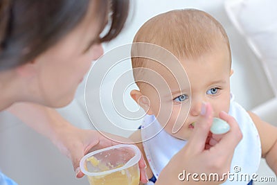 Woman spoon feeding baby from plastic pot food Stock Photo