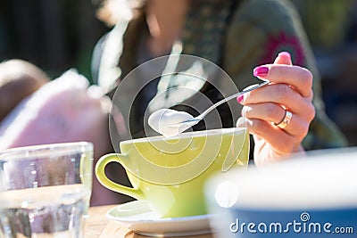 Woman spooning froth on a cappuccino as she sits outdoors Stock Photo