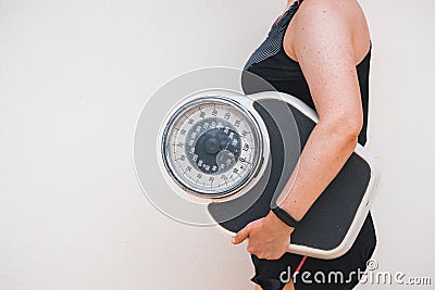 A woman in a sports outfit holds a professional scale under her arm, Concept, Spring weight loss, Healthy lifestyle, Positive Stock Photo