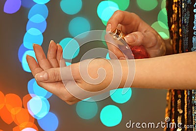 Woman spraying perfume on wrist against blurred lights Stock Photo