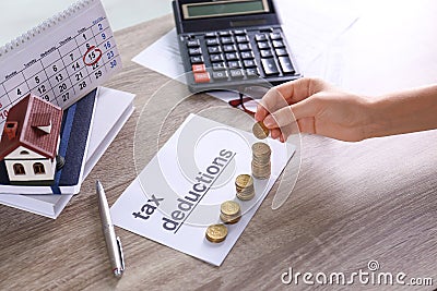 Woman stacking coins on paper with words TAX DEDUCTIONS at table Stock Photo
