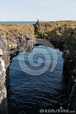 Woman stand on a natural stone gate by the ocean. Black volcanic rock cliff of western Icelandic coast Snaefellsnes Peninsula Icel Stock Photo