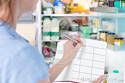 Woman Standing In Front Of Refrigerator In Kitchen With Notebook Writing Weekly Meal Plan Stock Photo