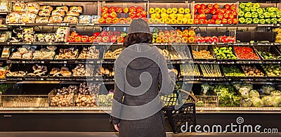 Woman standing in front of a row of produce in a grocery store. Stock Photo