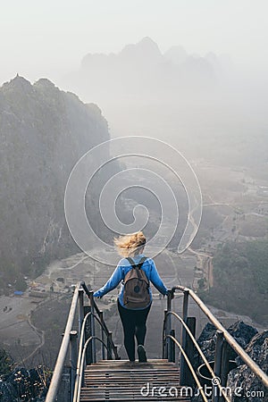 Woman standing on mountain peak with stairs going down during sunrise foggy morning in Hpa-An, Myanmar Stock Photo