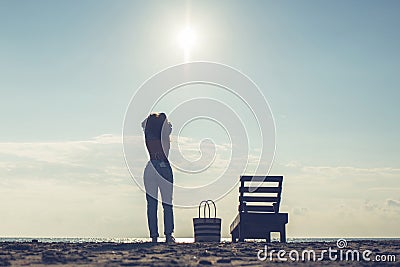 Woman standing near sun lounger and taking off her clother. Beach at sunset Stock Photo