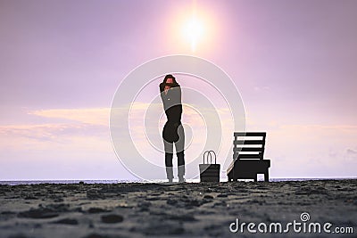 Woman standing near sun lounger and taking off her clother. Beach at sunset Stock Photo