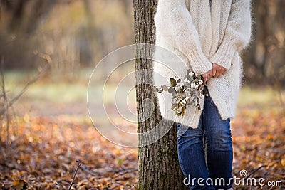 Woman standing near the tree and holding seasonal bouquet in her hands on a sunny autumn day in the park. Girl walking Stock Photo