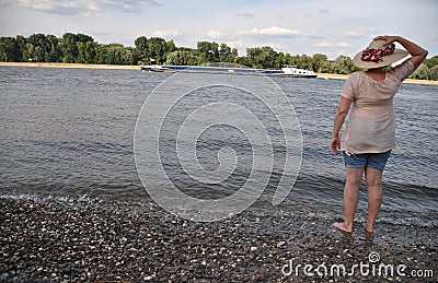 Woman standing at riverside looking out to water and passing river ship Editorial Stock Photo