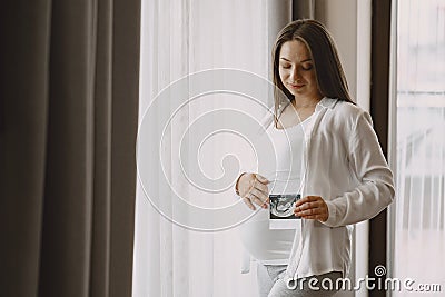 Pregnant woman stands by the window and looks at photo Stock Photo
