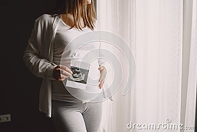 Pregnant woman stands by the window and looks at photo Stock Photo