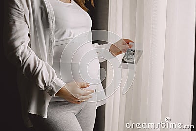 Pregnant woman stands by the window and looks at photo Stock Photo