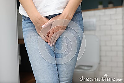 Woman stands in bathroom and covers her lower abdomen with her hand Stock Photo