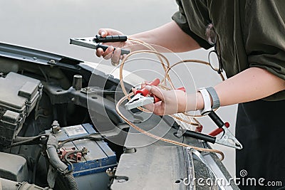Woman stands in front of a car with the hood open and holds the battery charging clamps Stock Photo