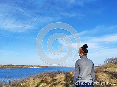A woman stands with her back to the camera, looks at the river, nature. Advertising space for spring Stock Photo