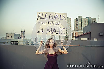 Woman stands on the roof with a poster `All girls are filled with Magic` International Womens Day concept. Stock Photo