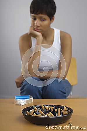 Woman Staring At Full Ashtray Of Cigarettes On Table Stock Photo