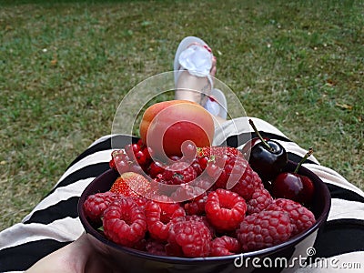 Woman in a striped dress sitting in the garden and eats fruits Stock Photo