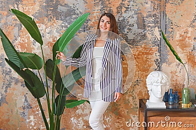 Woman in striped jacked posing in front of big plant. Indoor interior portrait Stock Photo