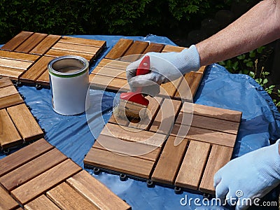 A woman strokes wood preservation glaze on square wood panels to make them weatherproof. Stock Photo