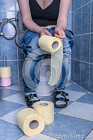 Woman suffers from diarrhea is sitting in restroom and holds toilet paper Stock Photo