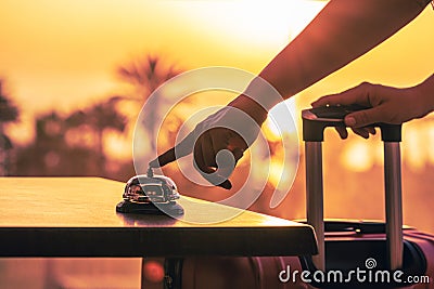 Woman with suitcase ringing hotel service bell with sea and palm tree view on sunset. Travel concept. 24-hour beach hotel front Stock Photo