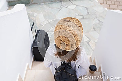 Woman with suitcase, straw hat and paper cup of coffee sits on the steps and waits for the owners of the apartment of the resort. Stock Photo