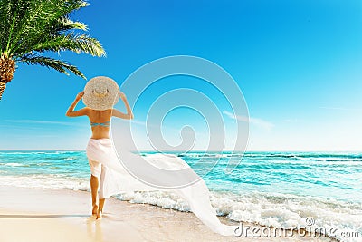 Woman Summer Beach Vacation. Travel Girl Sunbathing in Sun Hat, Bikini, White fluttering Dress. Women Back View looking at Ocean Stock Photo