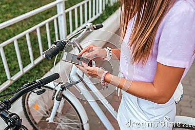 A woman summer stands bicycle, activates application buying rental bicycle in parking lot, in hands of phone. Online Stock Photo