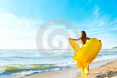 Woman on Sunny Sea Beach in Yellow Fluttering Dress, Fashion Model Back Rear View, Silk Cloth Waving on Wind Stock Photo