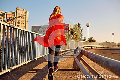 Woman super-hero runner in a red raincoat jogs. Stock Photo