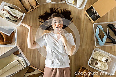 Woman surrounded by shoes in plastic container and cardboard box shopaholism and storage organizing Stock Photo