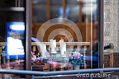 A woman at a table in a restaurant. View through the window. Street reflections in the glass Editorial Stock Photo
