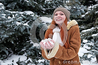 Woman take a handful snow in winter park at day. Fir trees with snow. Stock Photo