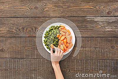 Woman take some carrots and beans lie on a plate Stock Photo