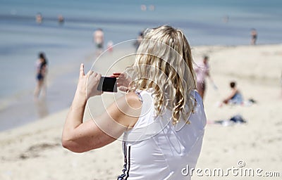 A woman takes a picture with her cell in Arenal beach Editorial Stock Photo