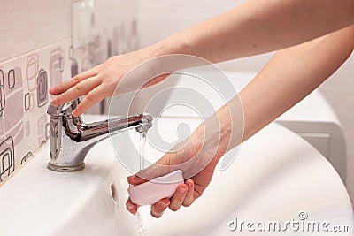 A woman takes a soap and opens a water tap to wash her hands in a white sink in the bathroom. Stock Photo