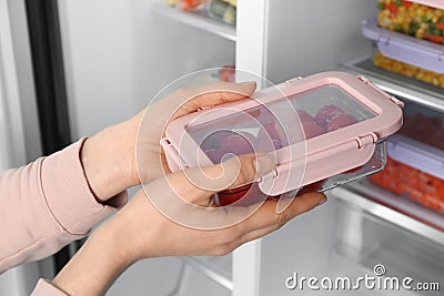 Woman taking container with frozen tomatoes from refrigerator Stock Photo